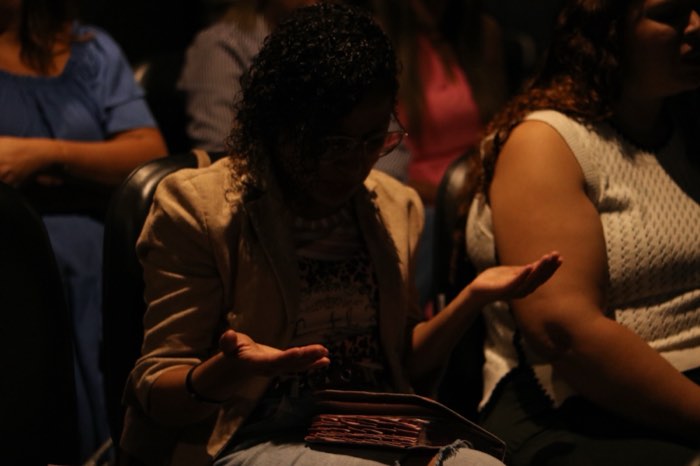 Bíblia no colo e mãos estendidas durante a Palavra